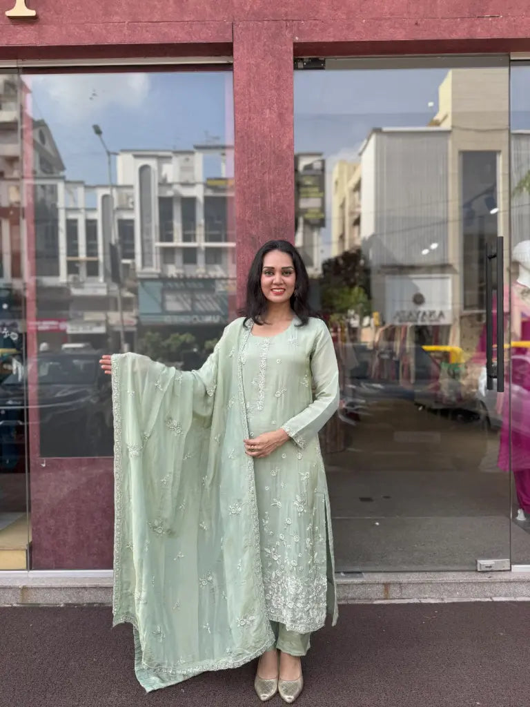Woman in a light green traditional outfit standing in front of a Ethonique store with glass doors.