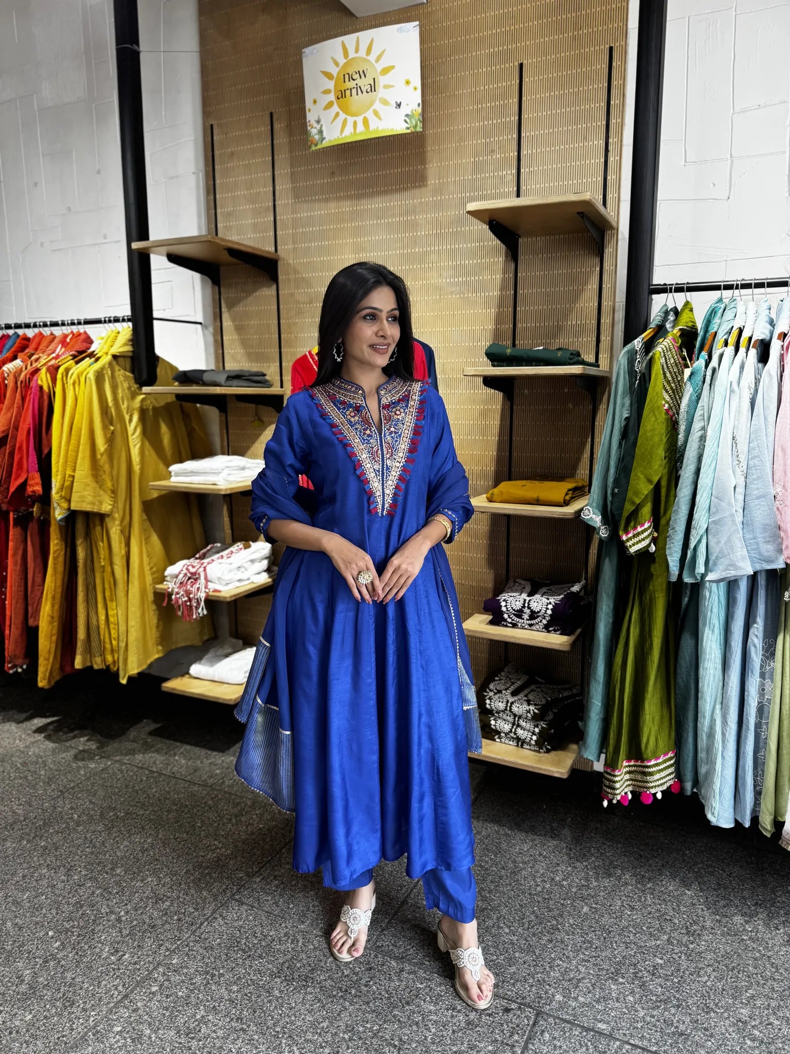 A woman modeling a royal blue cotton kurta with colorful embroidered detailing on the neckline, standing inside a clothing store.