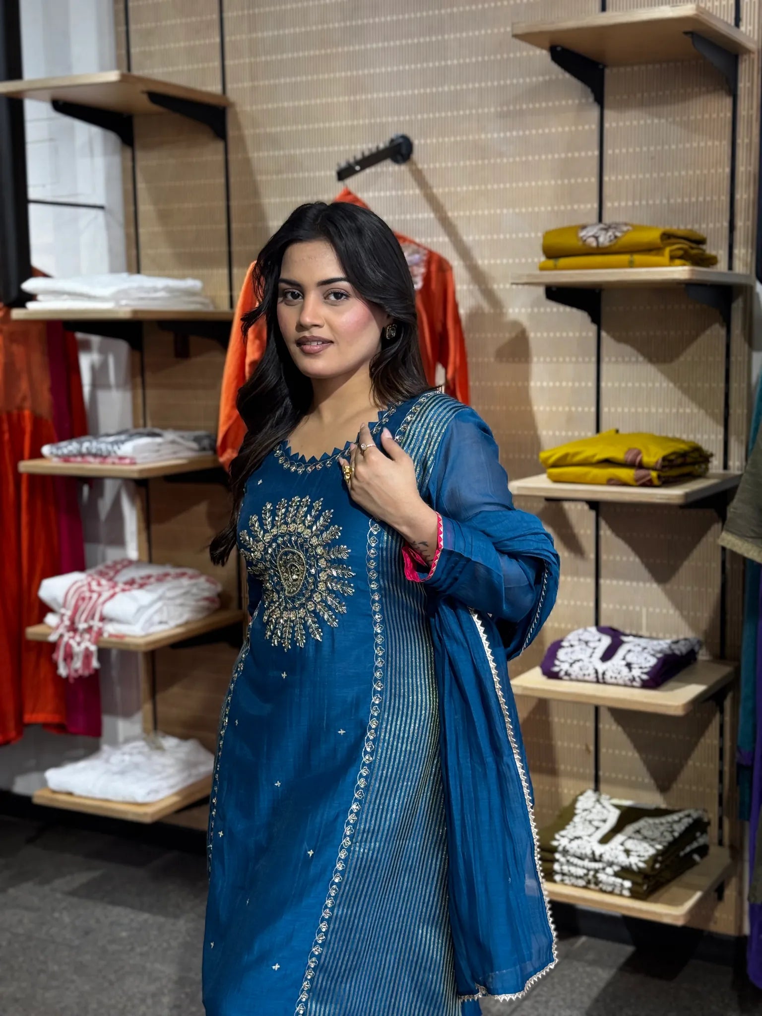 Close view of the petrol-blue kurta's yoke, a dense gold medallion stitched above a row of fine vertical stripes.