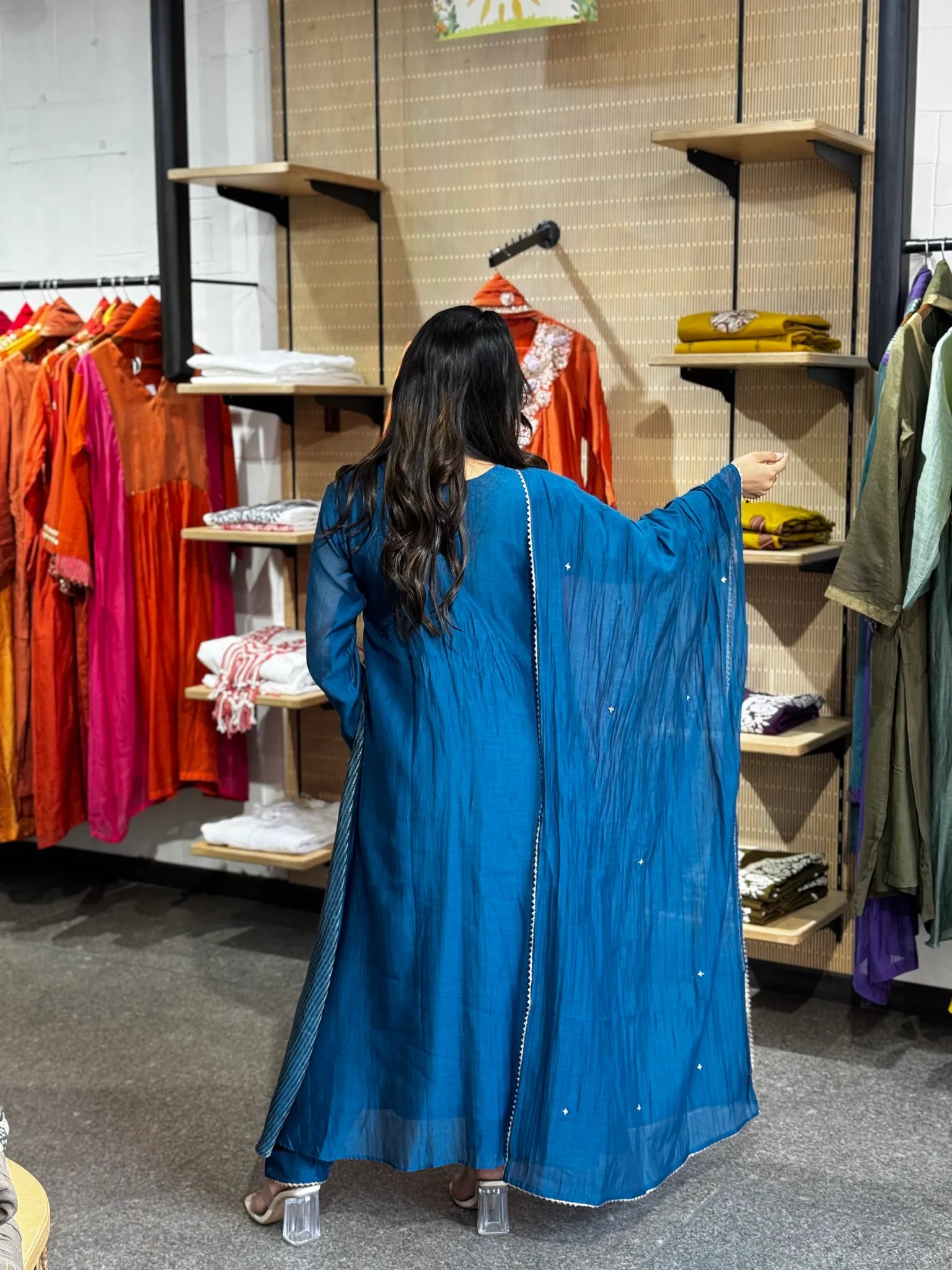Back view with the petrol-blue dupatta opened out to one side, its gold-dotted edge catching the boutique lighting.
