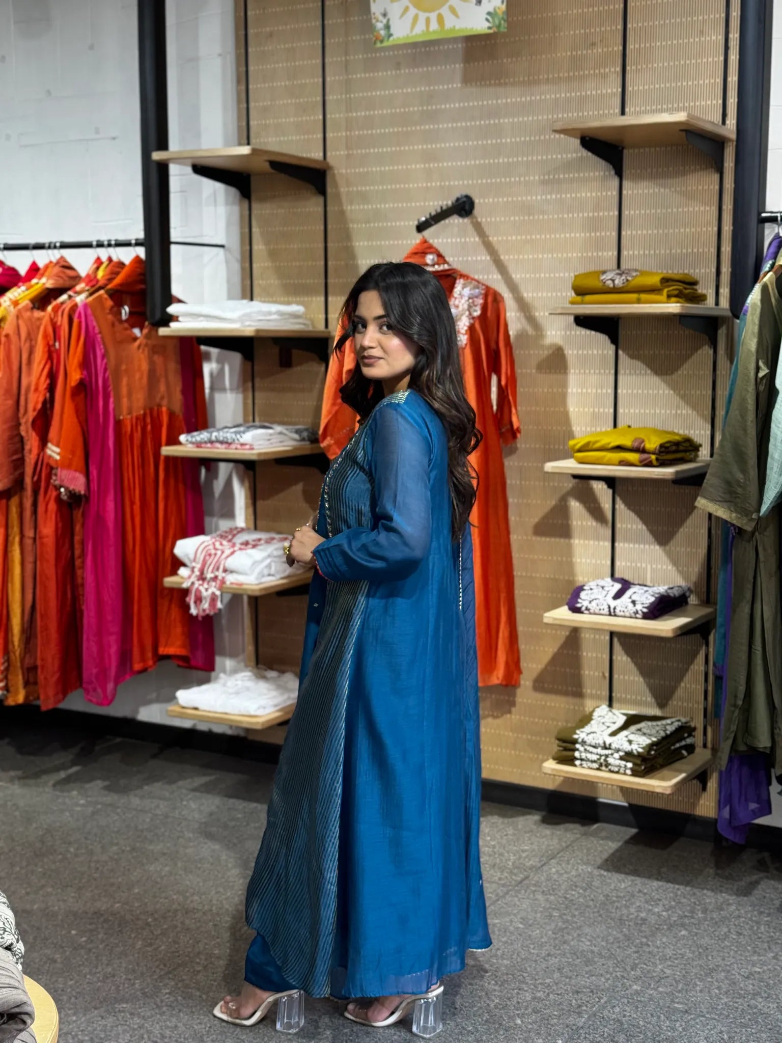 Turning to the side in petrol blue, the dupatta gathered at the elbow and the gold medallion yoke catching light.