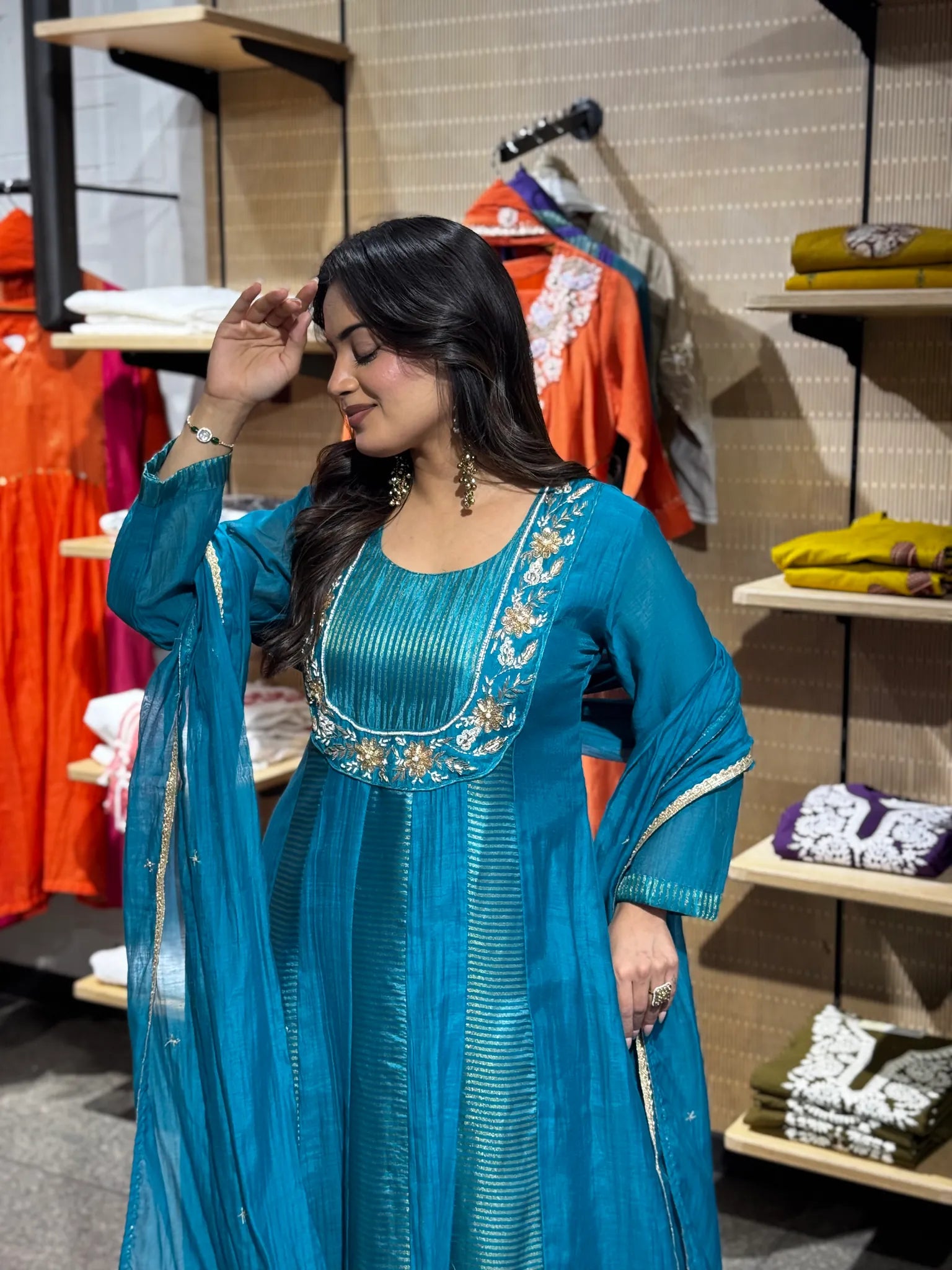 Arm lifted so the sheer turquoise dupatta opens out, showing the gold-worked floral yoke of the kurta beneath it.
