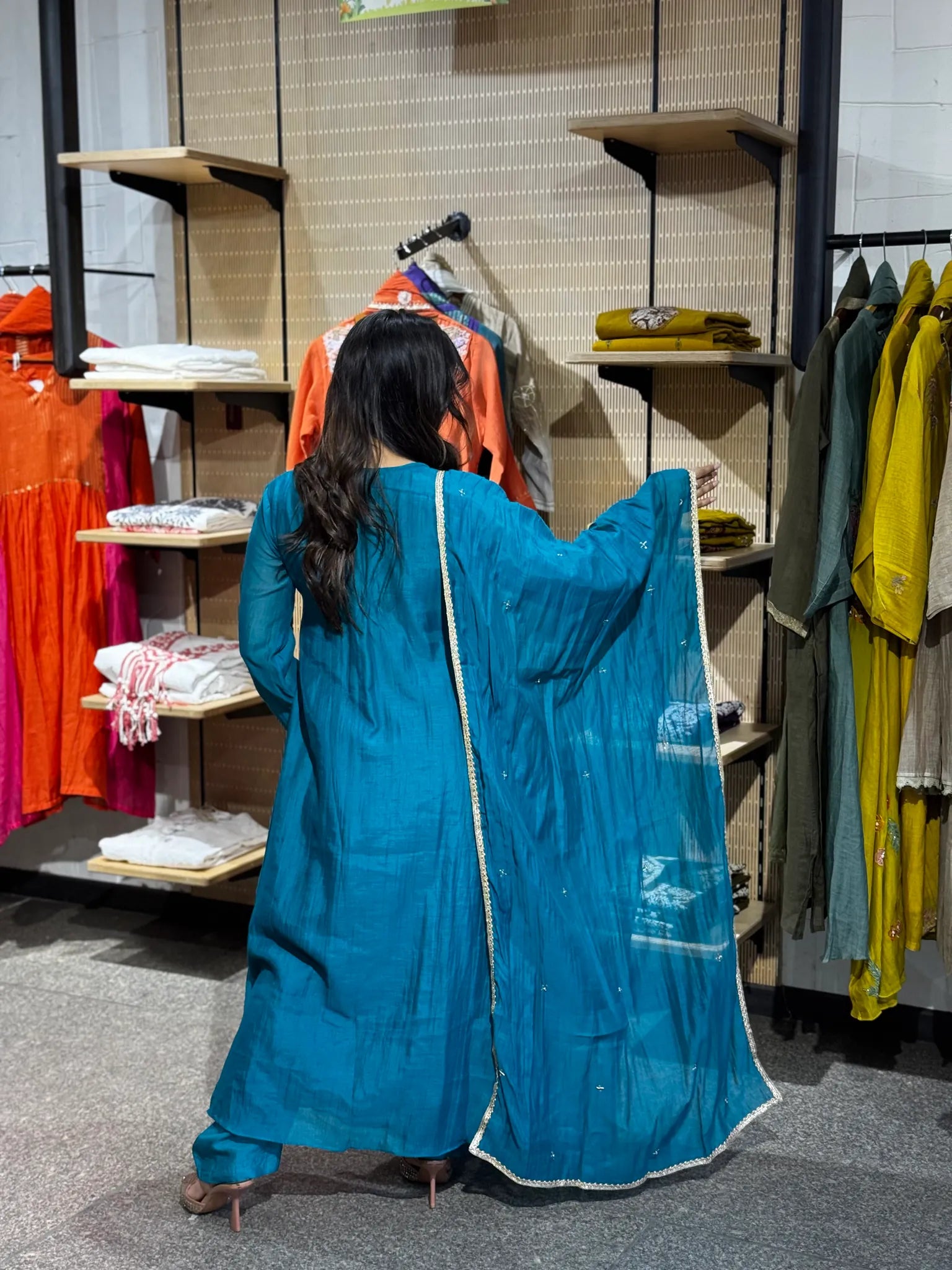 Back view of the turquoise set, with the gold-edged dupatta held wide open against the boutique's wooden shelves.