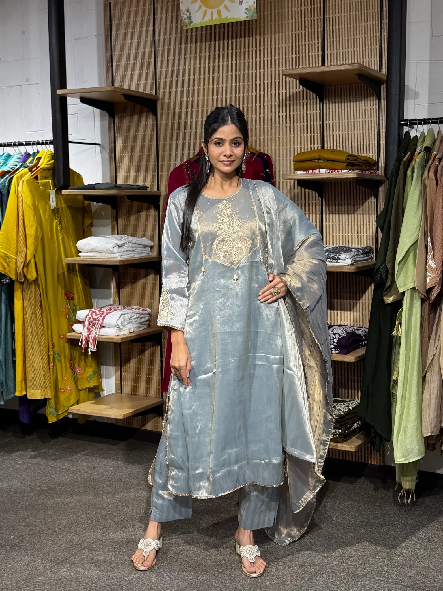 A woman modeling a pale blue tissue straight cut kurta pant set with a matching dupatta, standing inside a clothing boutique.