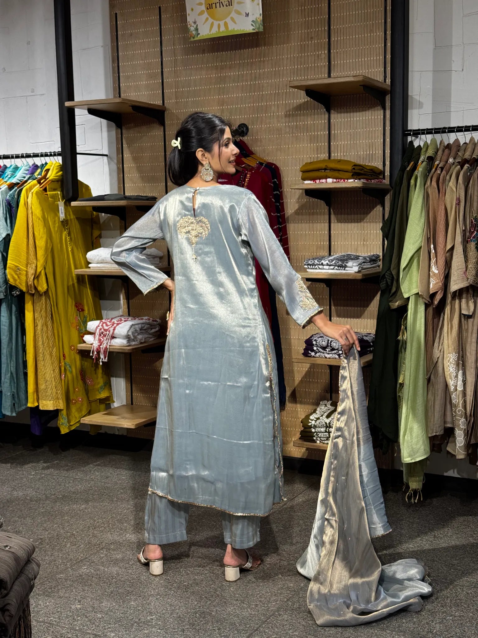 Back view of a pale blue tissue straight cut kurta and matching pants, the model holding the dupatta open to show its gold border.