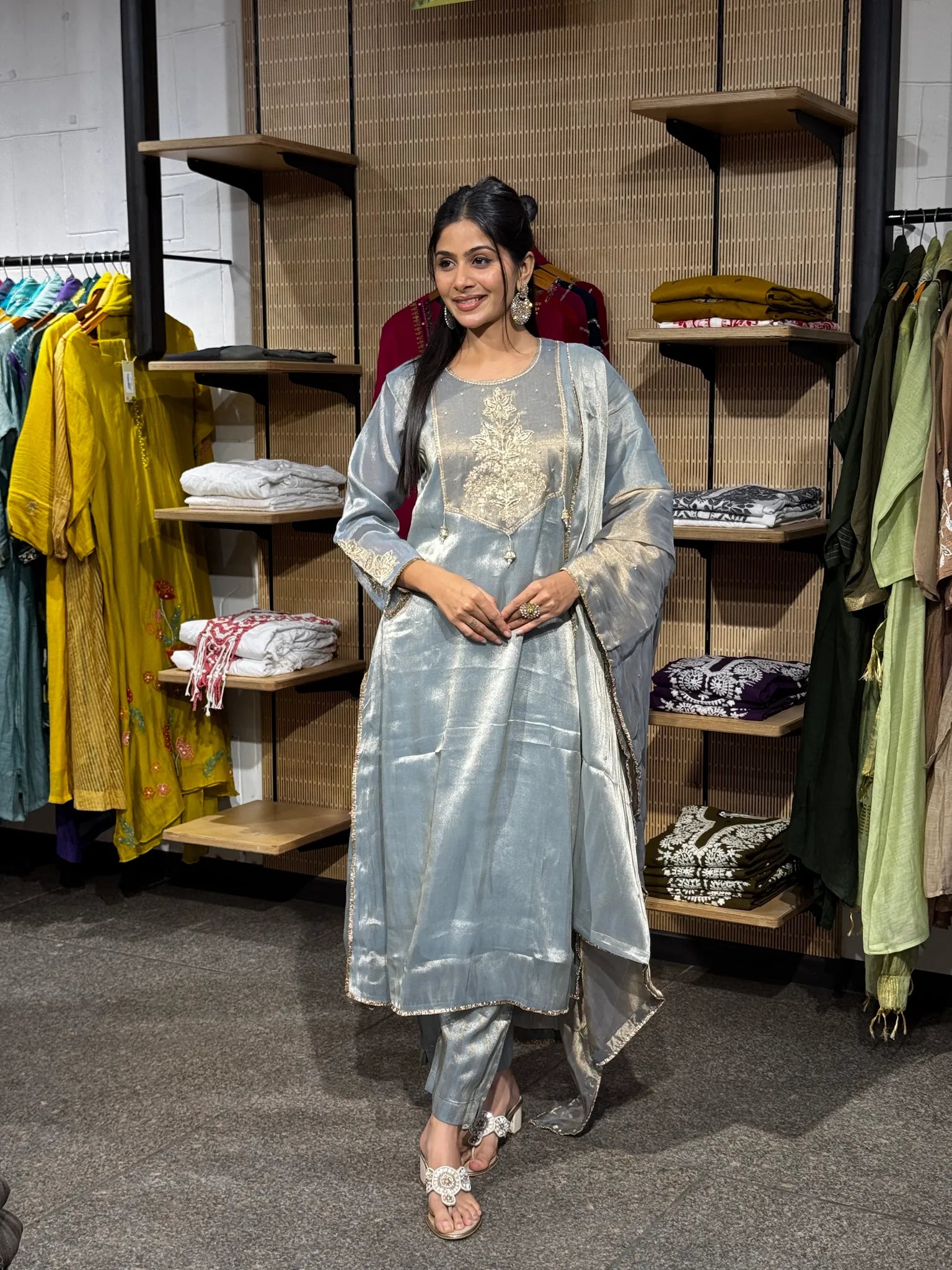 A woman modeling a pale blue tissue straight cut kurta pant set with the dupatta draped over one shoulder, in a boutique.