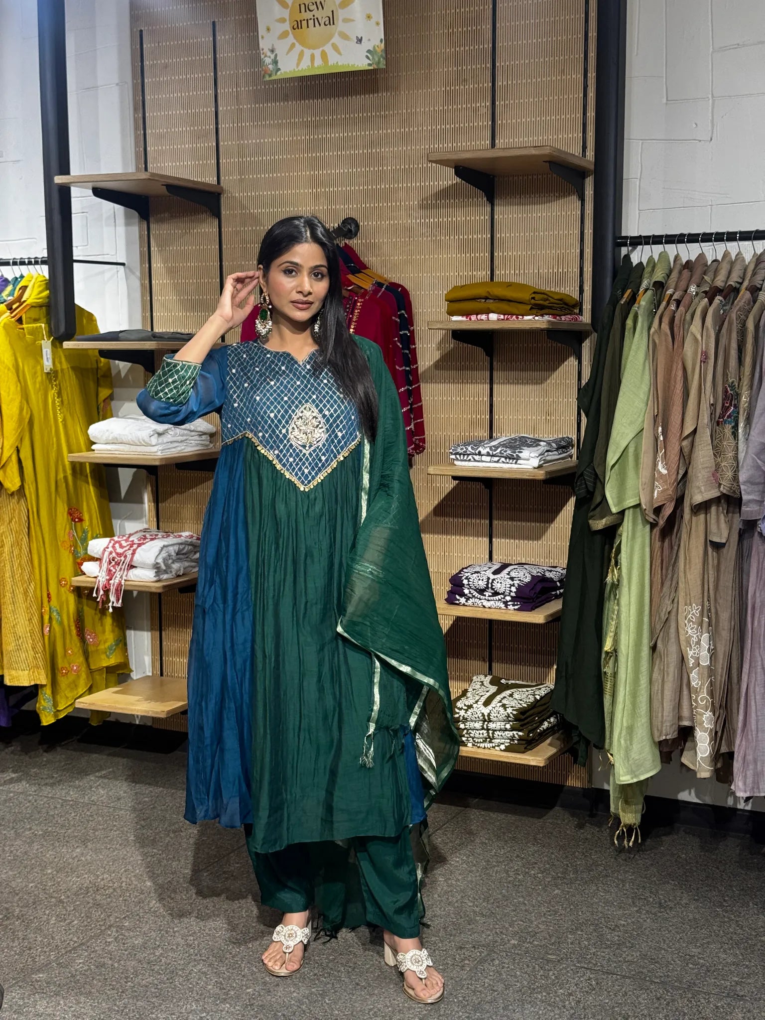 A woman modeling a teal green mul chanderi A-line kurta pant set with matching pants, standing in a boutique.