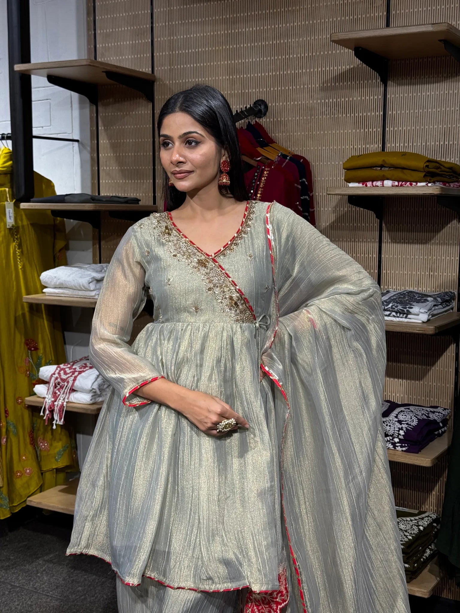A woman wearing a cream tissue kediya sharara suit with a flared peplum top and wide sharara, inside a clothing store.