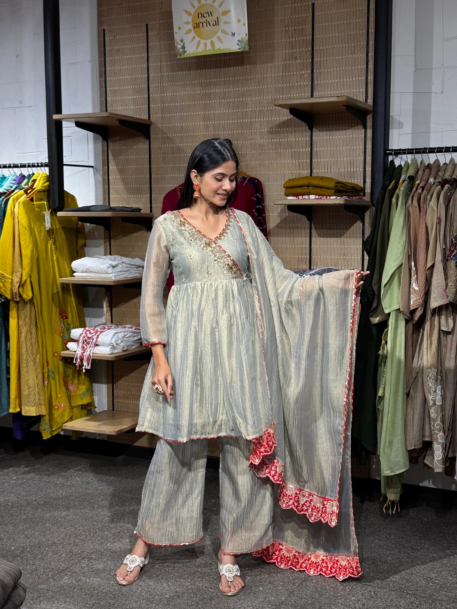 A woman modeling a cream tissue kediya sharara suit with the embroidered dupatta draped over one shoulder, in a boutique.