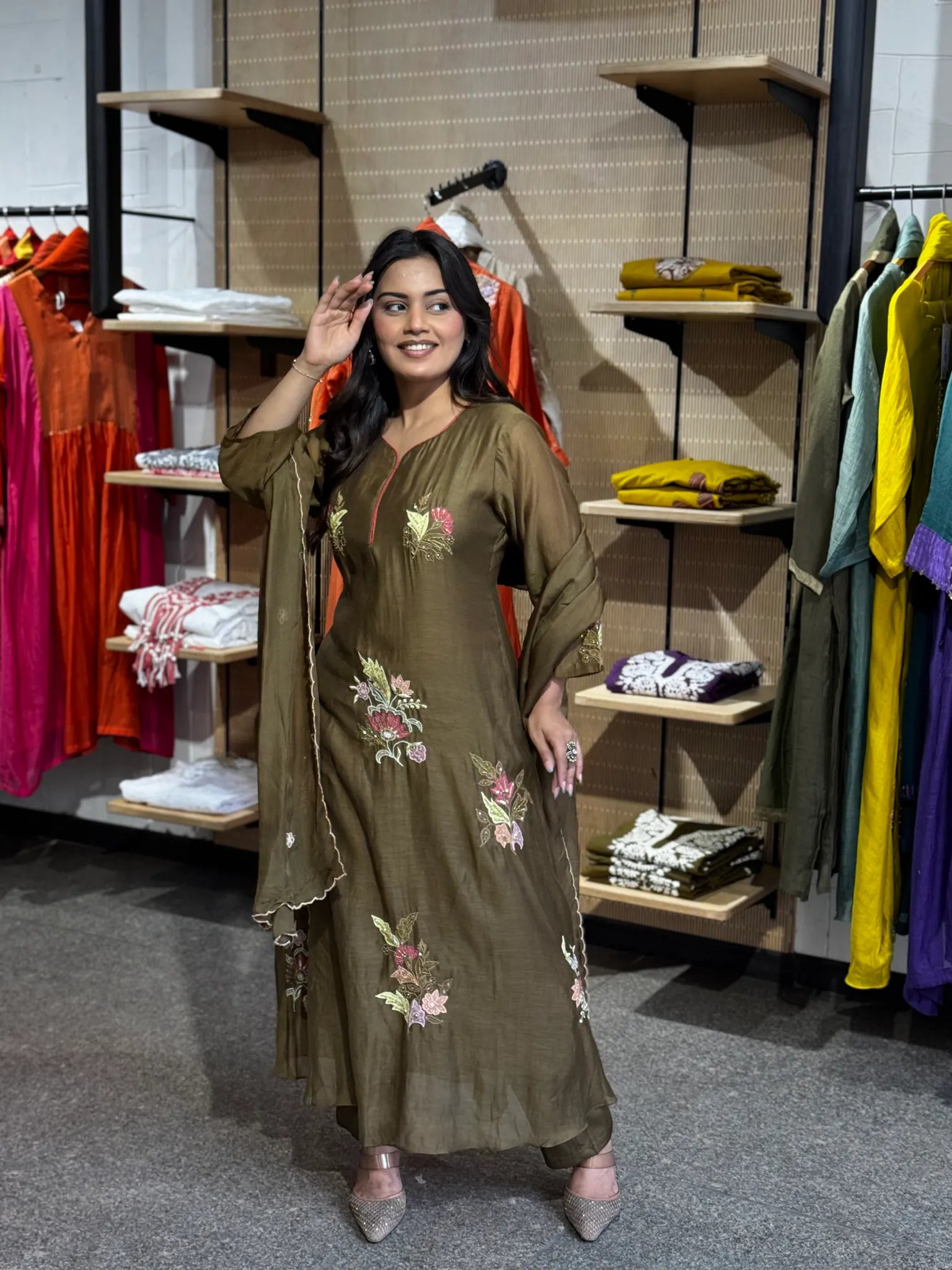 Full-length olive kurta and matching palazzo, model lifting a hand to her hair, embroidered blooms scattered down the softly falling panel.