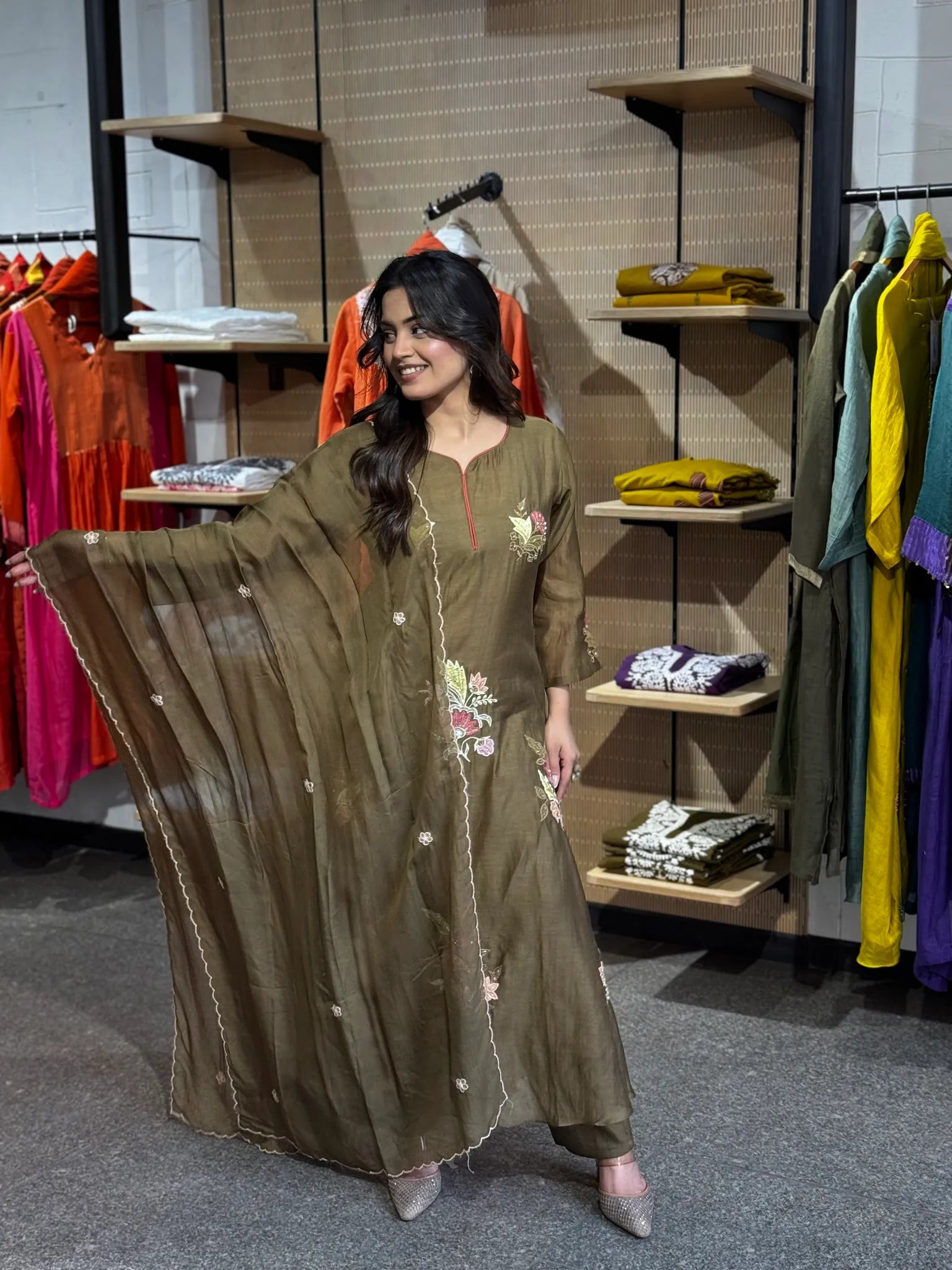 The sheer olive dupatta swept wide open, its scalloped ivory edge catching light against the boutique's wooden shelving.