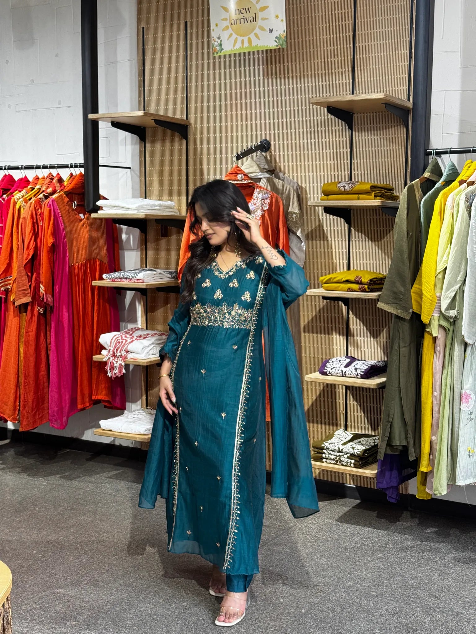 Full-length teal set, model touching her hair, the gold-bordered dupatta running the length of the flared kurta.