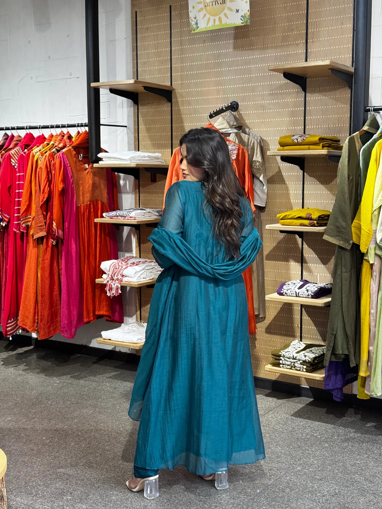 Back view of the teal anarkali, the sheer dupatta falling straight to the hem against the boutique's wooden shelves.