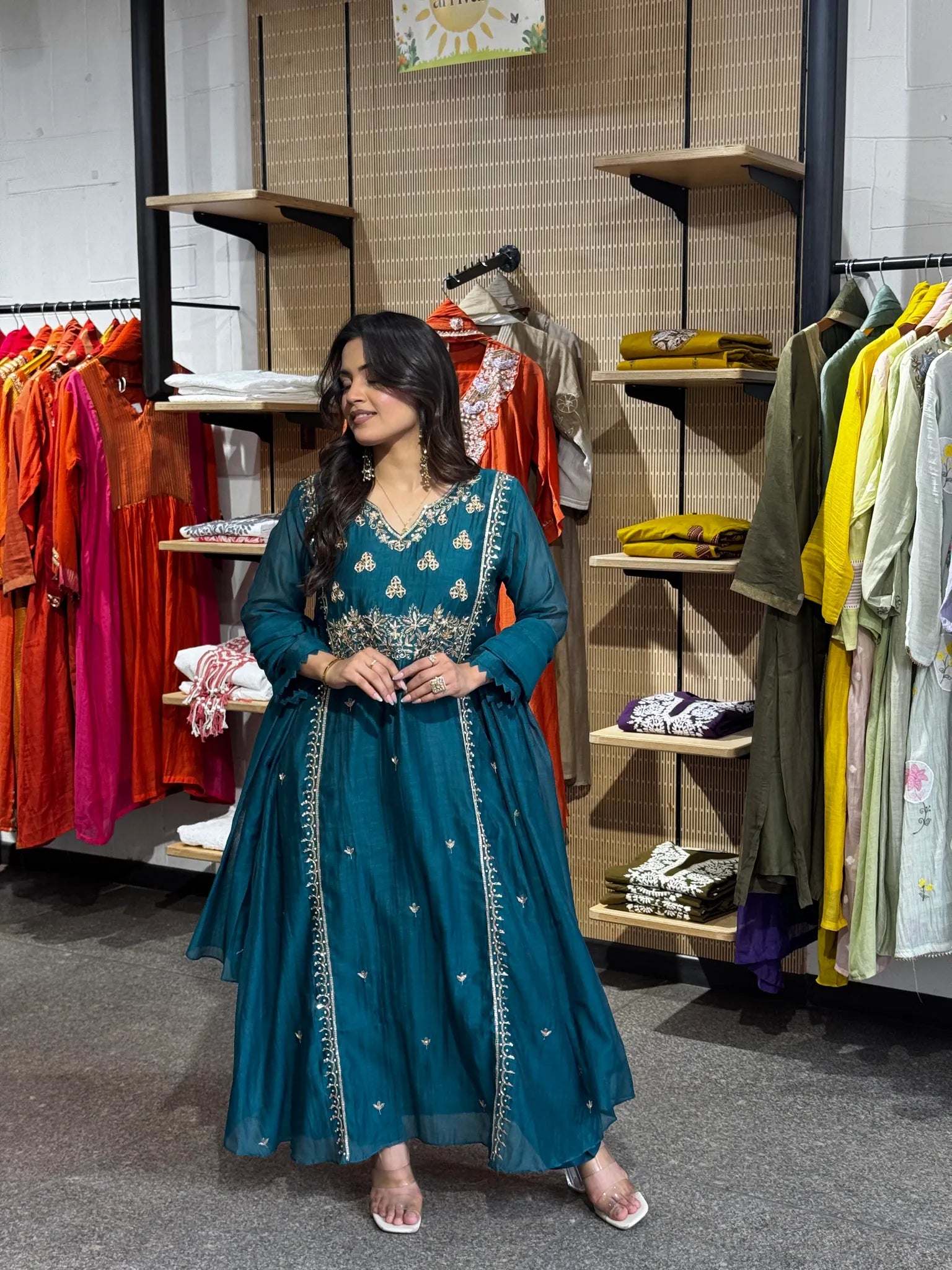 Standing front-on in the teal set, hands clasped, the A-line kurta flaring wide over matching narrow trousers.