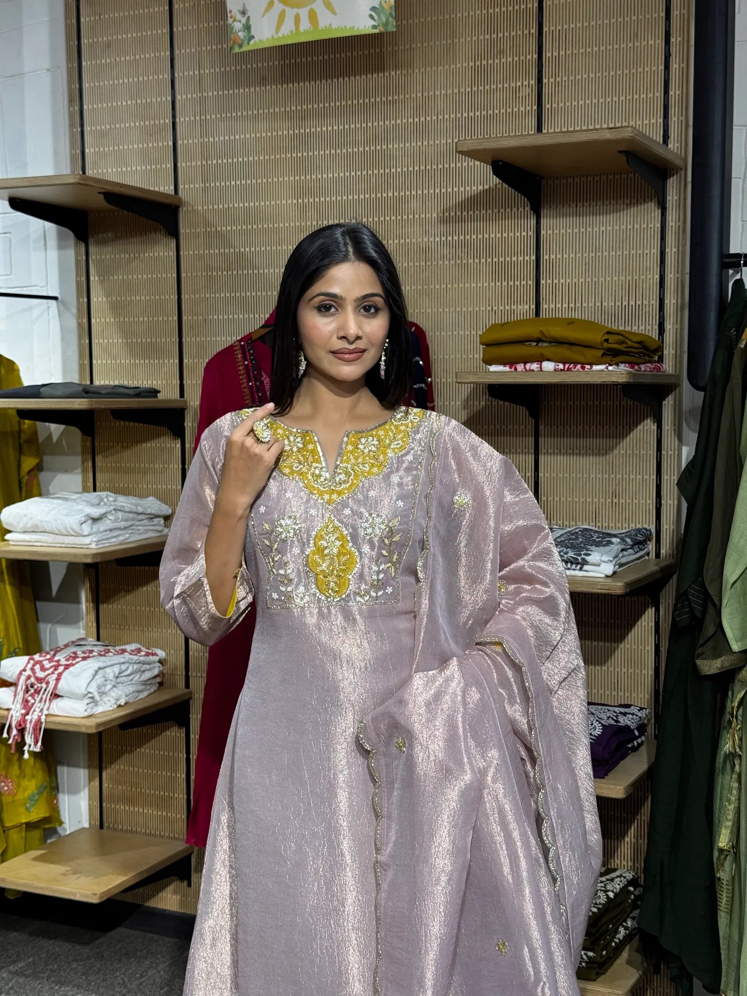 Close view of a woman in a lilac tissue kurta with a yellow and gold embroidered neckline, one hand raised to the collar.