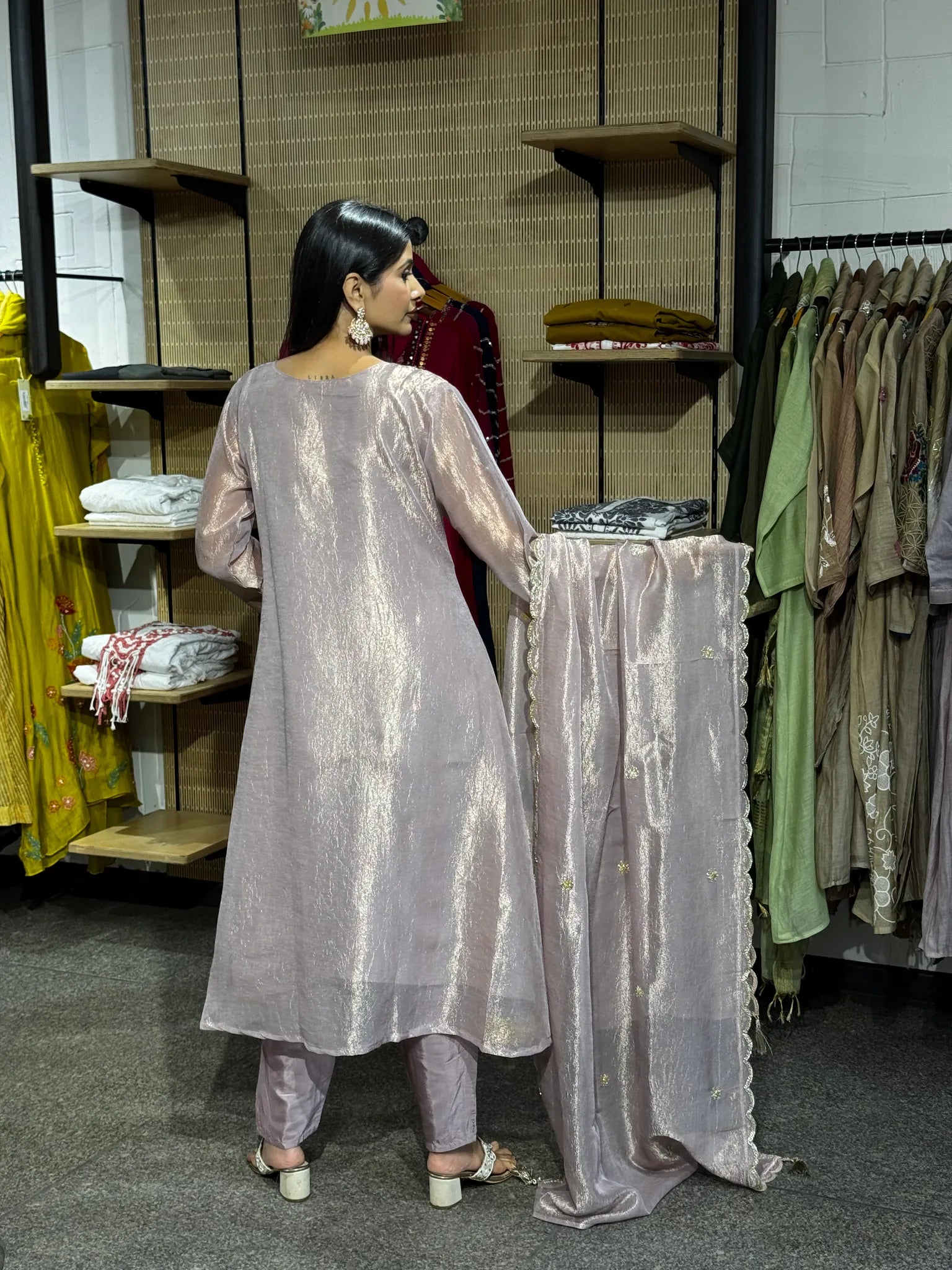Back view of a lilac tissue A-line kurta and matching pants, the model holding the dupatta open to show its gold border.