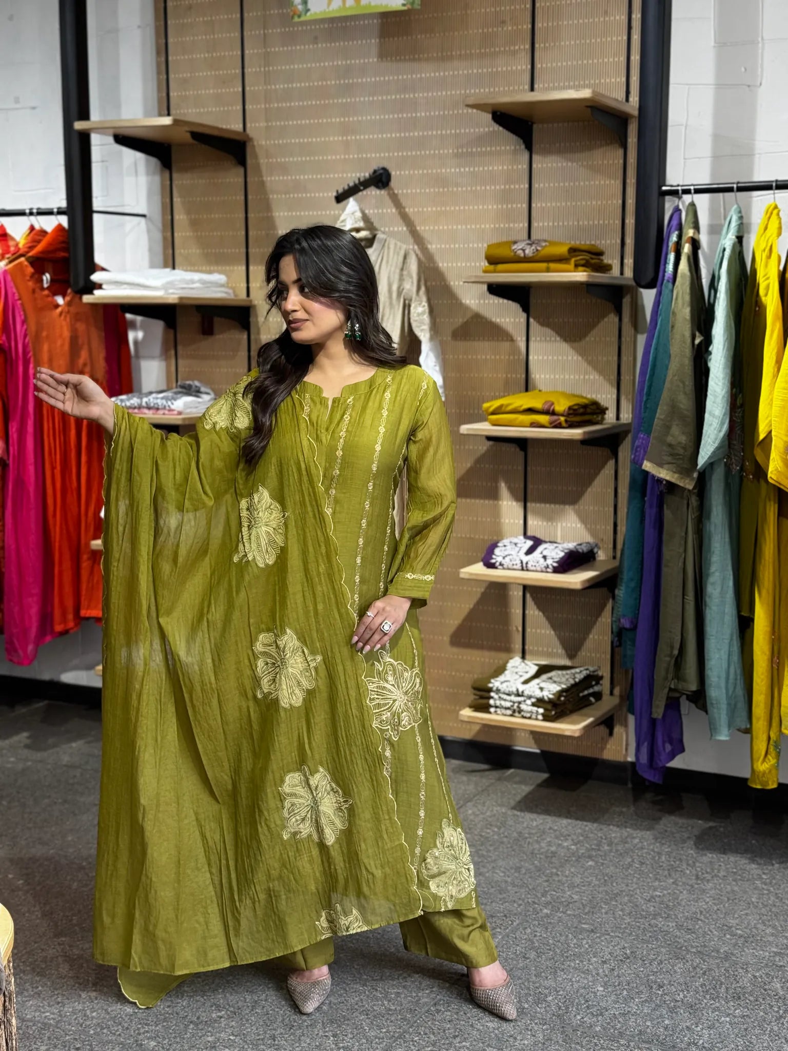 Mehendi-green chanderi kurta worked with large cream blooms, dupatta over the arm and bright boutique rails behind.
