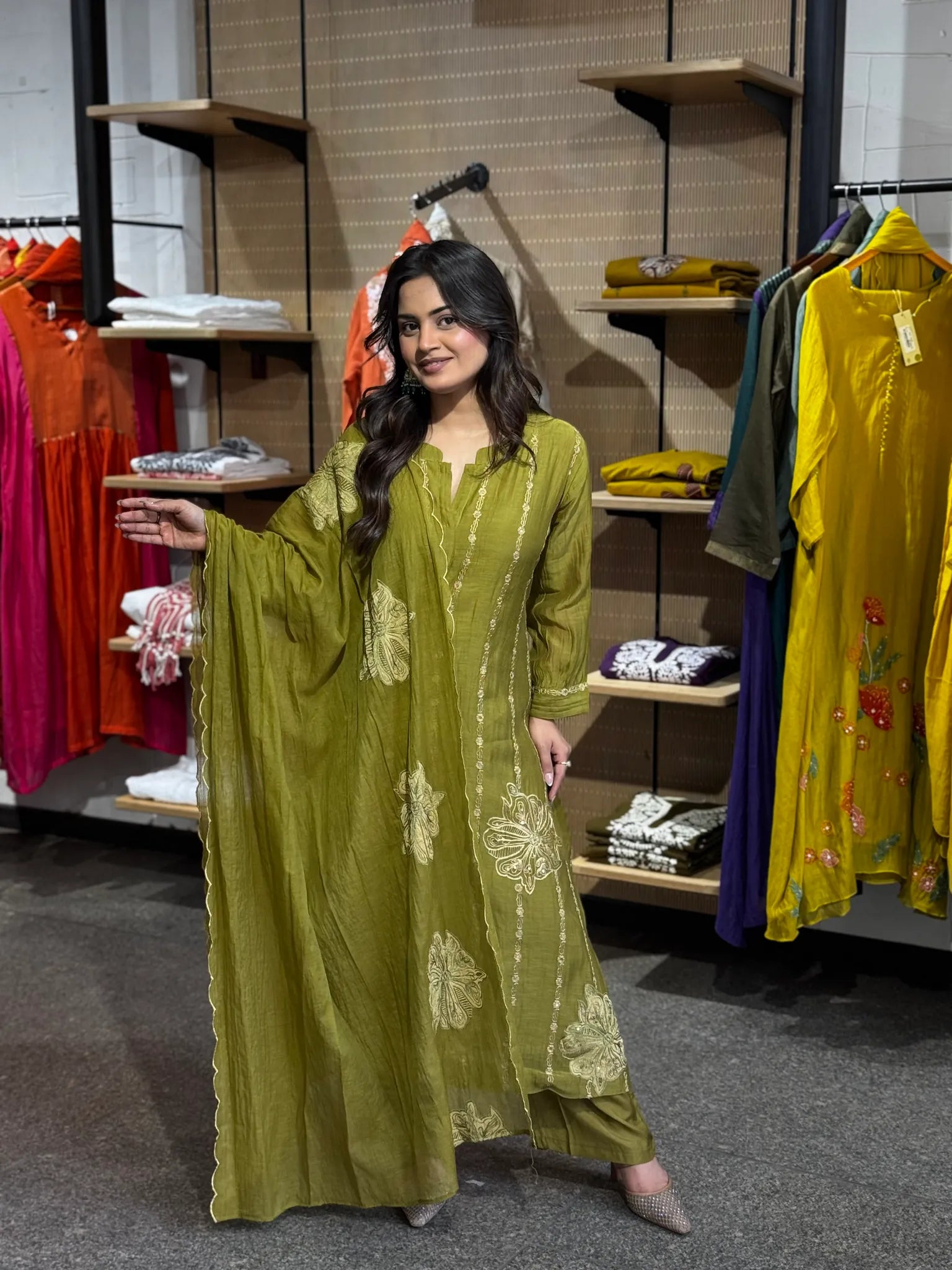Full-length mehendi green set, model reaching out a hand, cream floral motifs running down the kurta and palazzo.
