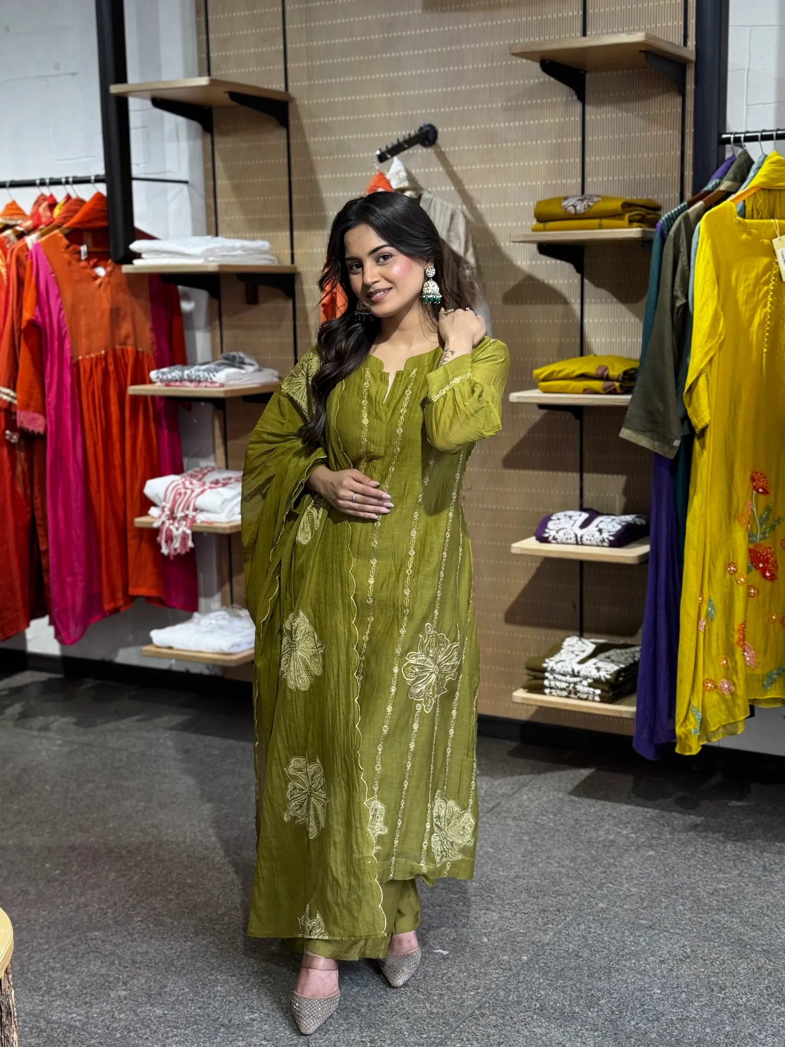 Model in mehendi green with the dupatta gathered at her waist, ivory blooms scattered across the front panel of the kurta.