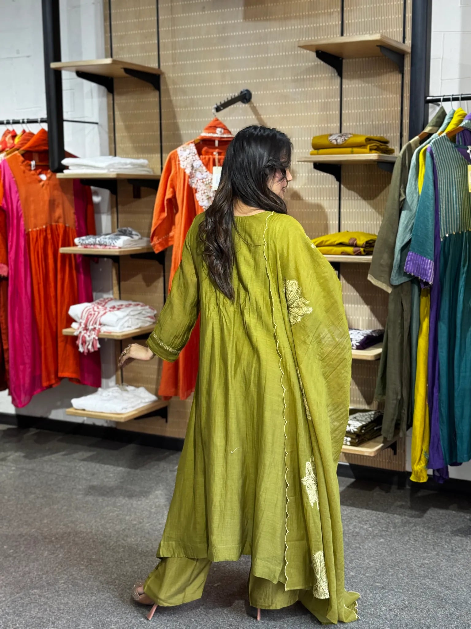 Turning side-on in mehendi green, the cream floral work visible along the dupatta and down the hem of the kurta.