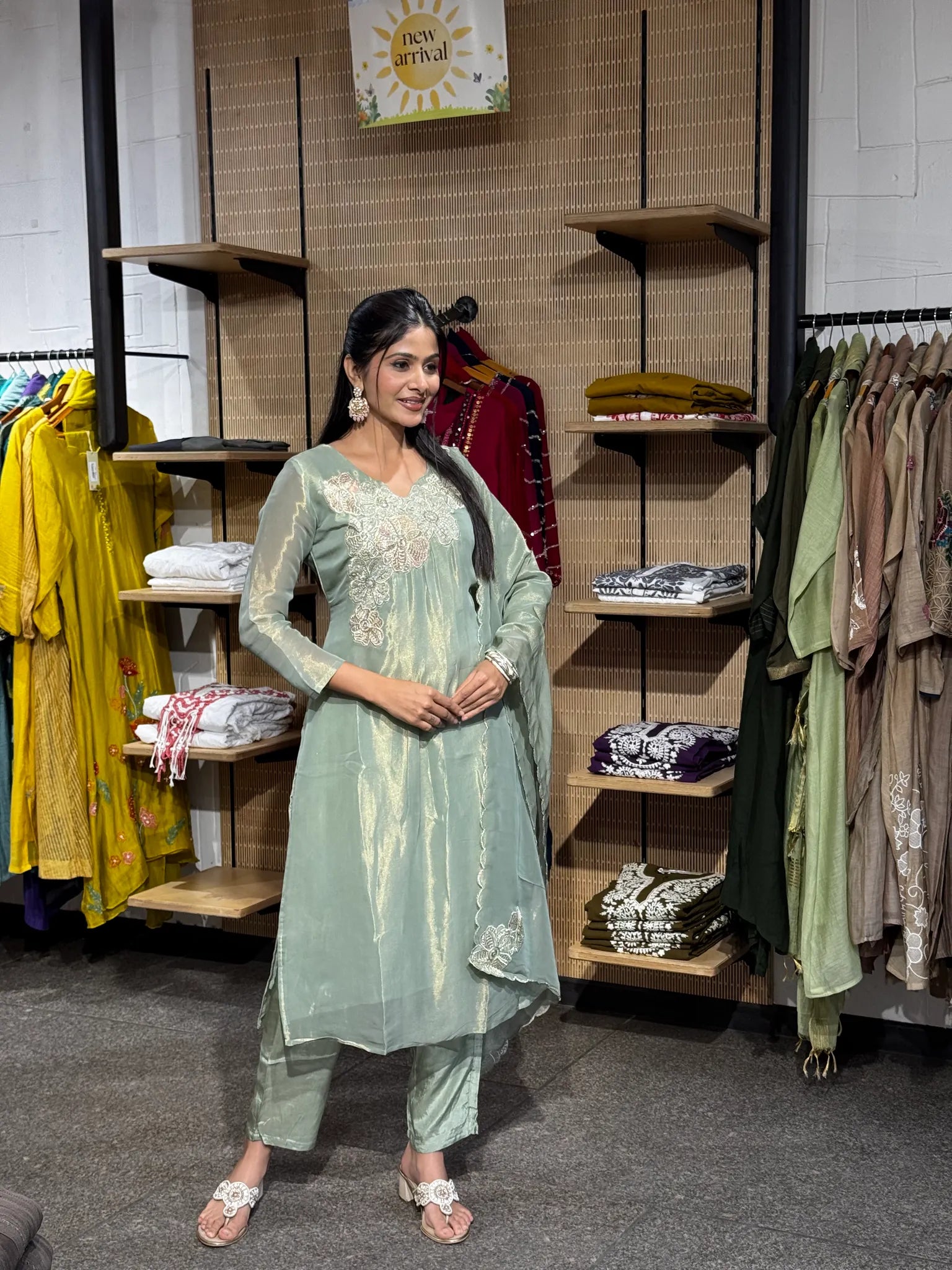 A woman modeling a mint green tissue A-line kurta pant set with the dupatta draped across both shoulders, standing in a boutique.