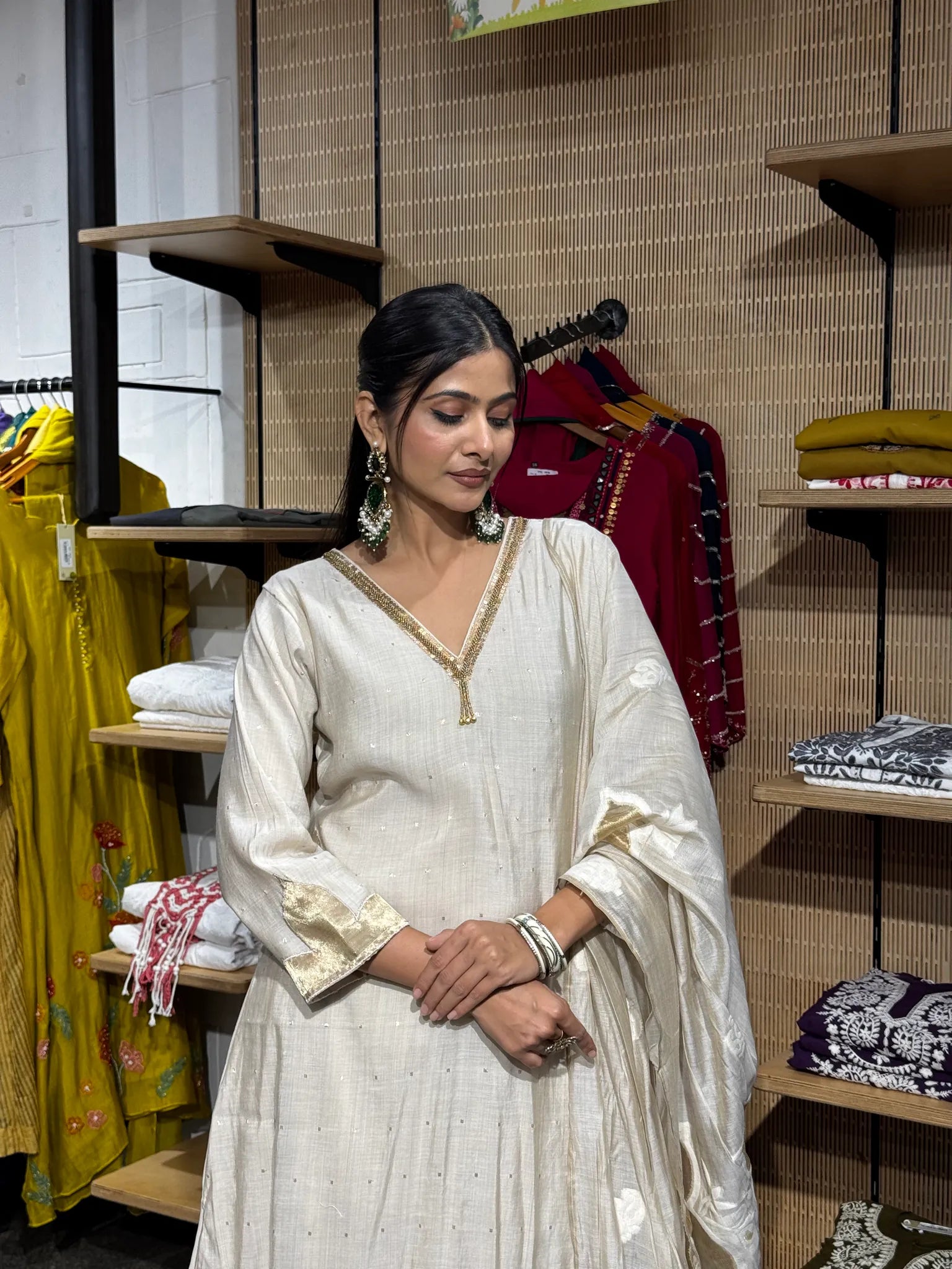 Close view of an off white mul chanderi kurta with a gold piped V-neck and tassel, worn with a gold-bordered dupatta.