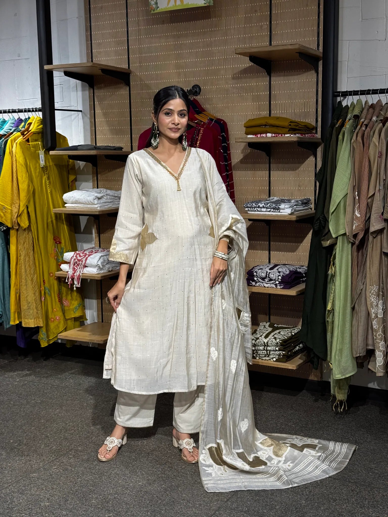 A woman wearing an off white mul chanderi A-line kurta and matching pants with the dupatta over one shoulder, inside a clothing store.