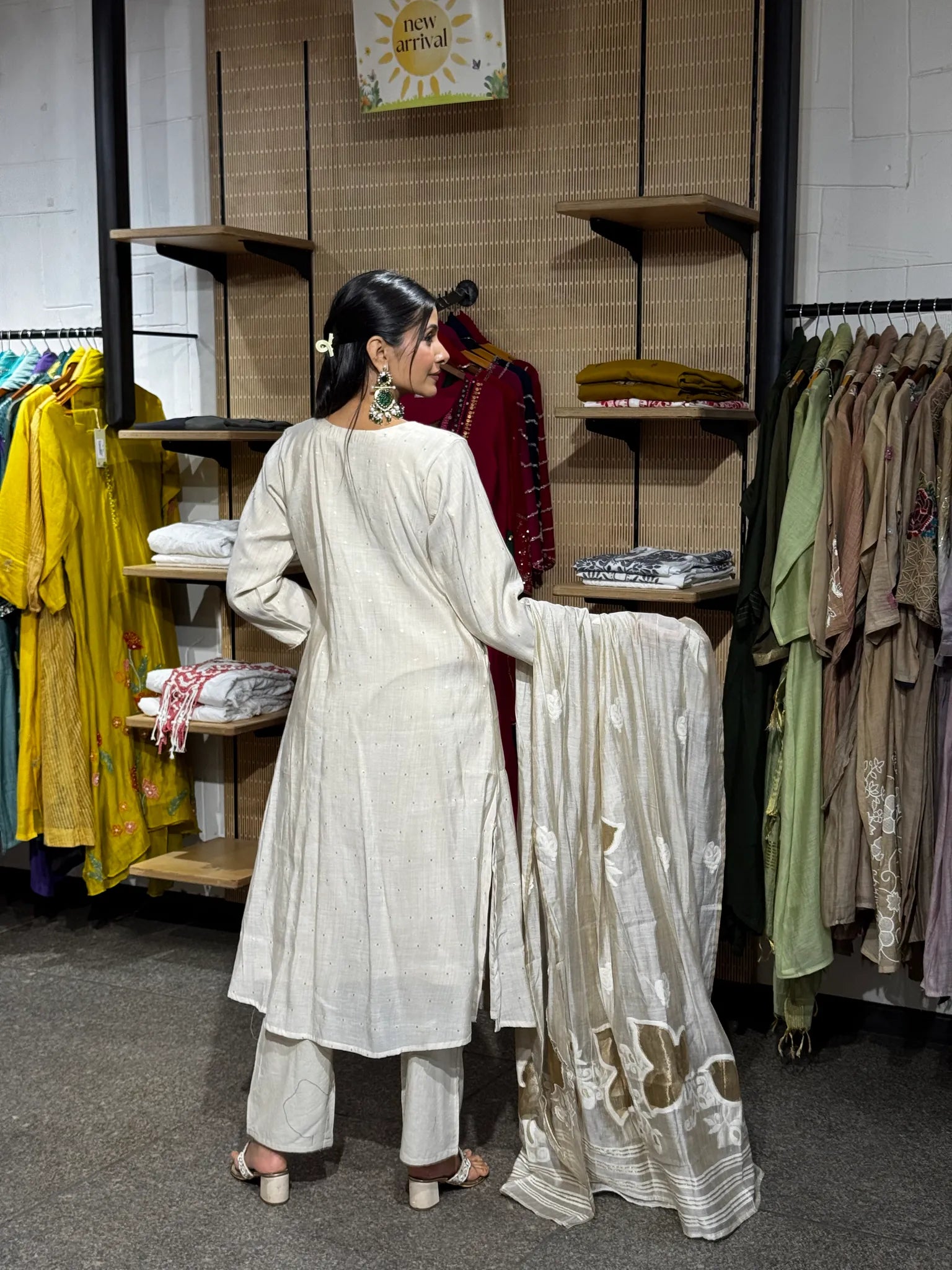 Back view of an off white mul chanderi A-line kurta pant set, the model holding the dupatta open to show its woven stripe border.