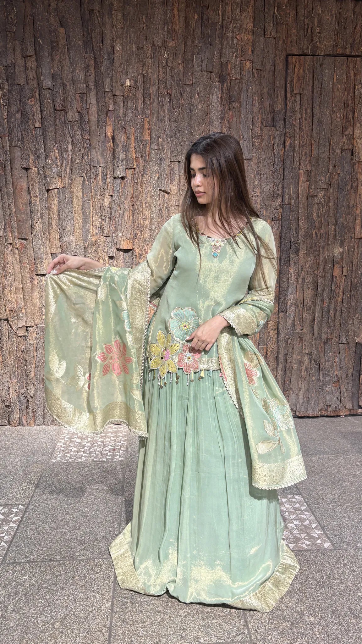 The gold zari dupatta held open to show its woven border, with floral thread embroidery scattered across the pista green tissue kurta.