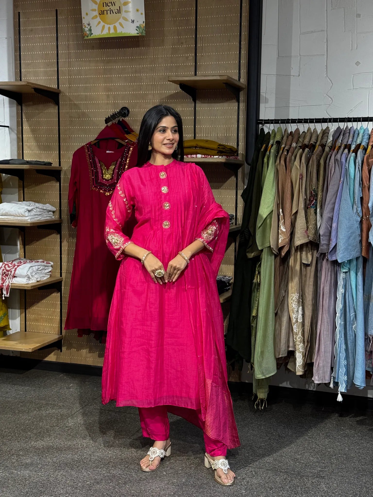 A woman modeling a rani pink mul chanderi A-line kurta pant set with a matching dupatta, standing inside a clothing boutique.