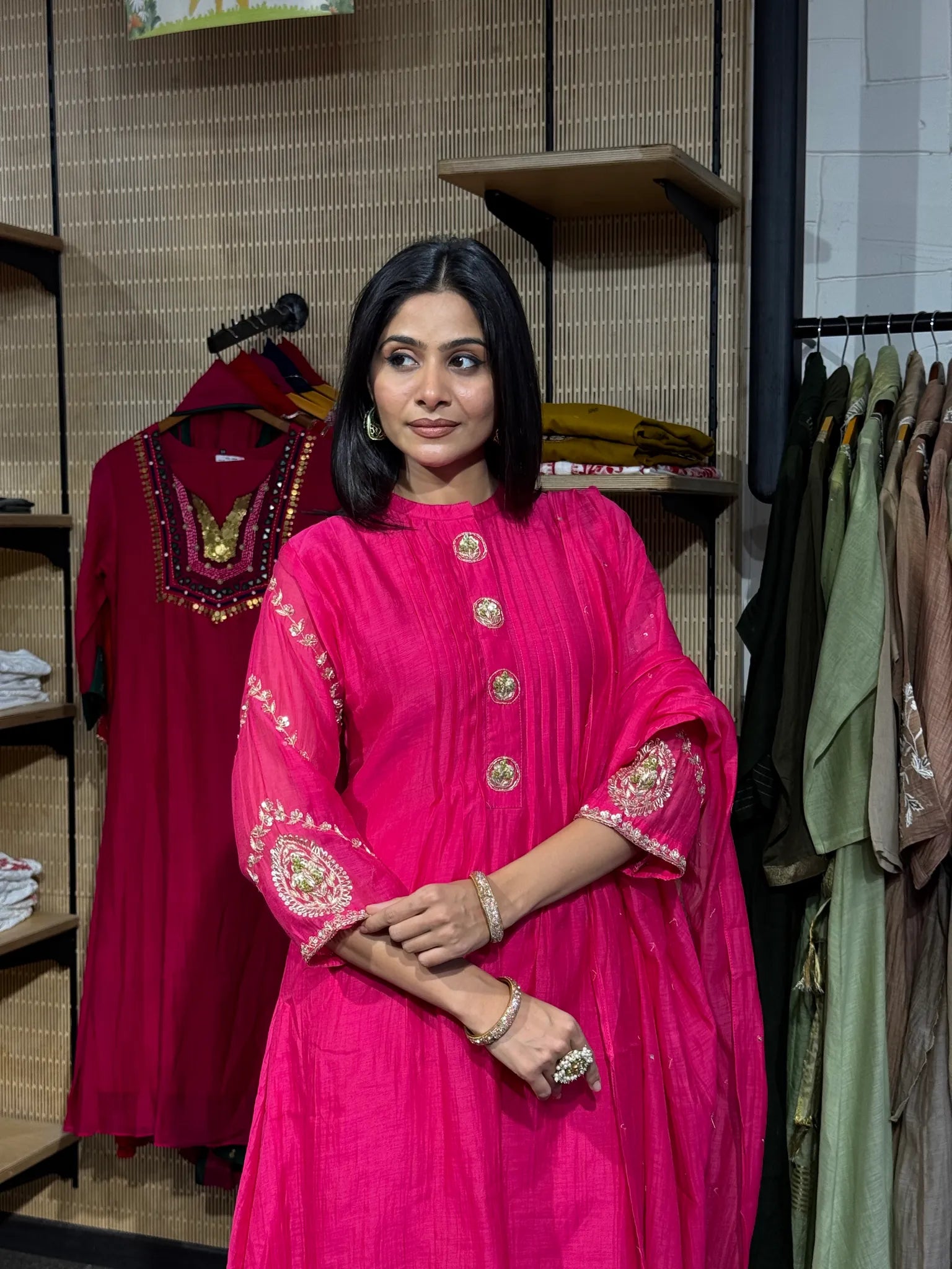 Close view of a rani pink mul chanderi kurta with a stand collar, gold buttons and gold embroidered sleeve borders.