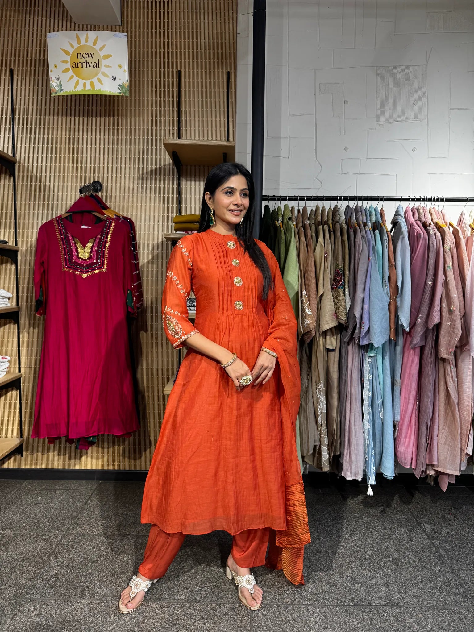 A woman modeling a rust orange mul chanderi A-line kurta pant set with a matching dupatta, standing inside a clothing boutique.
