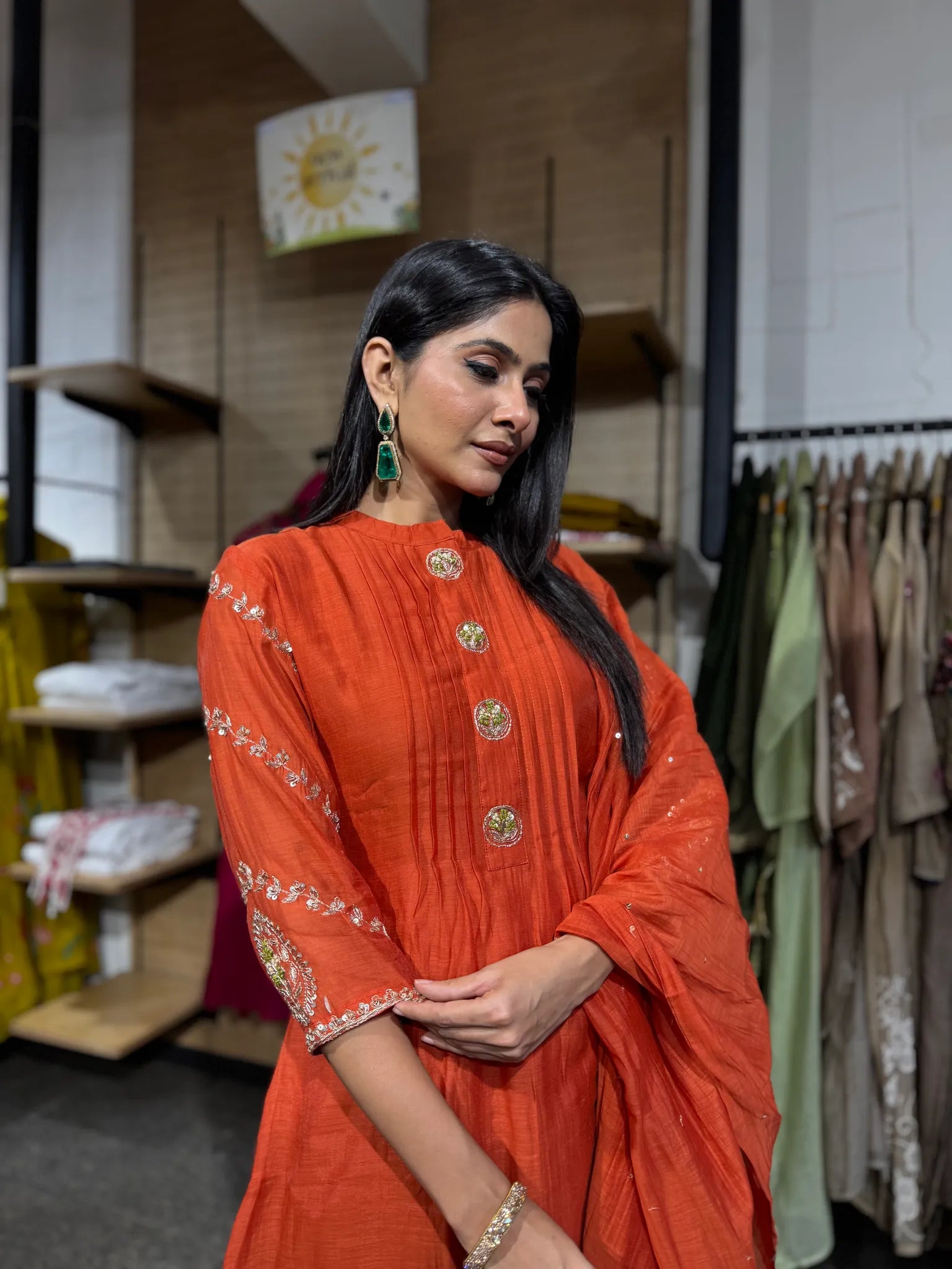 Close view of a rust orange mul chanderi kurta with a stand collar, gold buttons and embroidered sleeve borders.