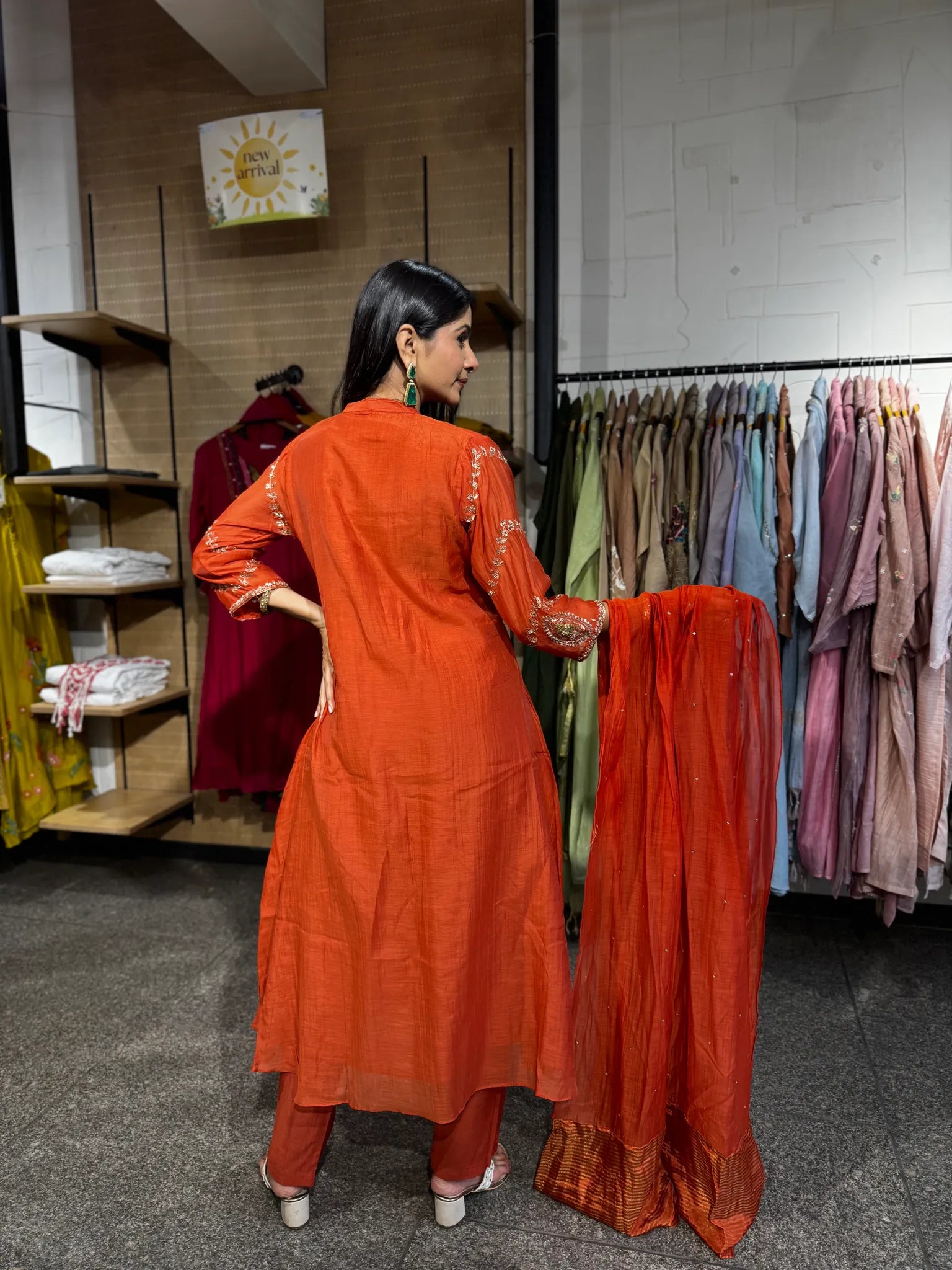 Back view of a rust orange mul chanderi A-line kurta pant set, the model holding the dupatta open to show its zari border.