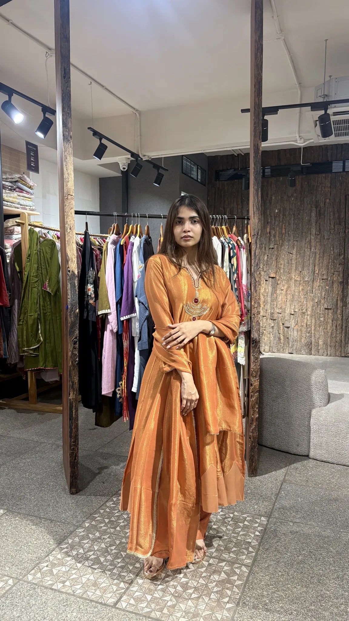 Front view of the rust orange A-line kurta with its matching pant, the tissue dupatta gathered over one forearm.