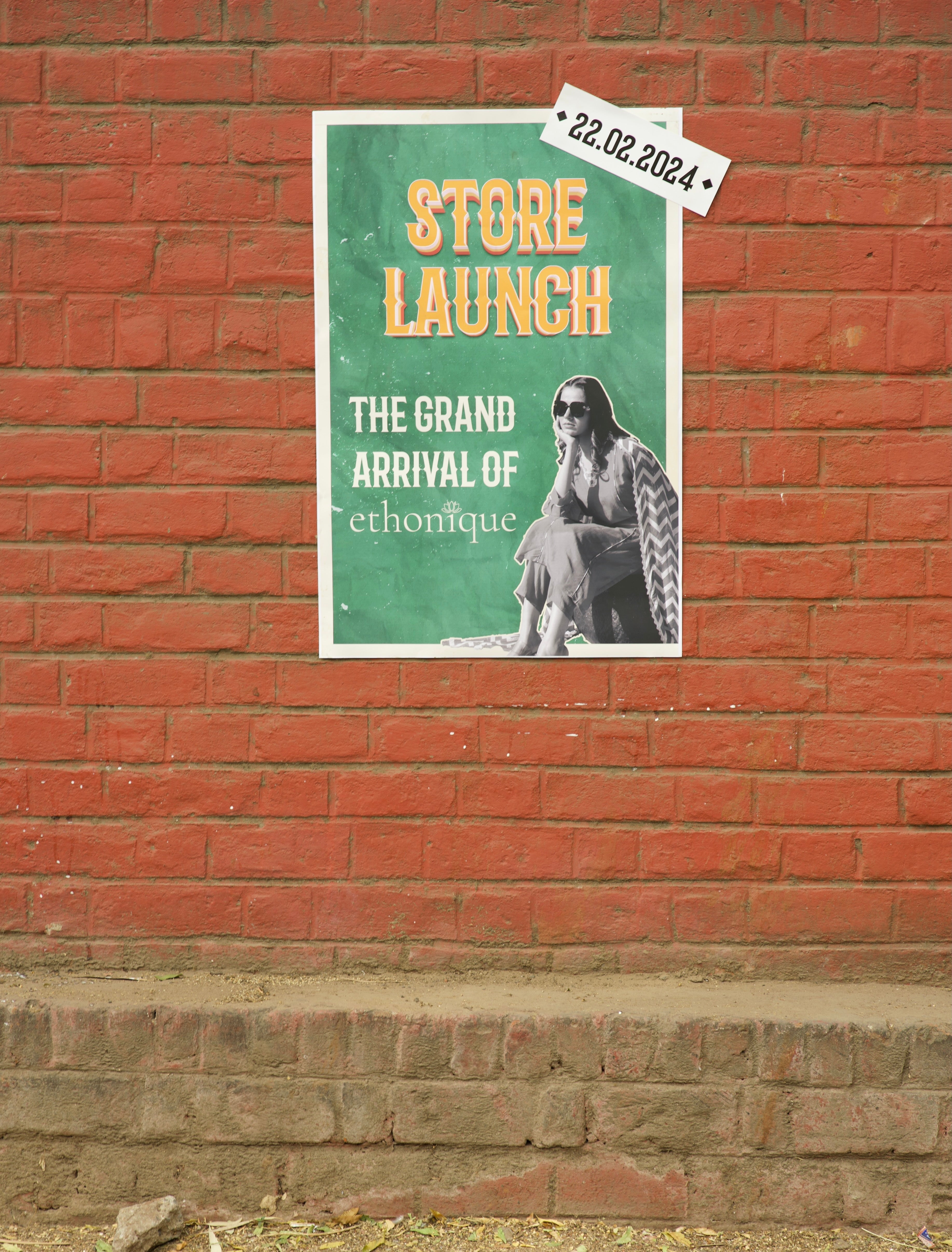 Poster for a store launch on a brick wall with text and a date.