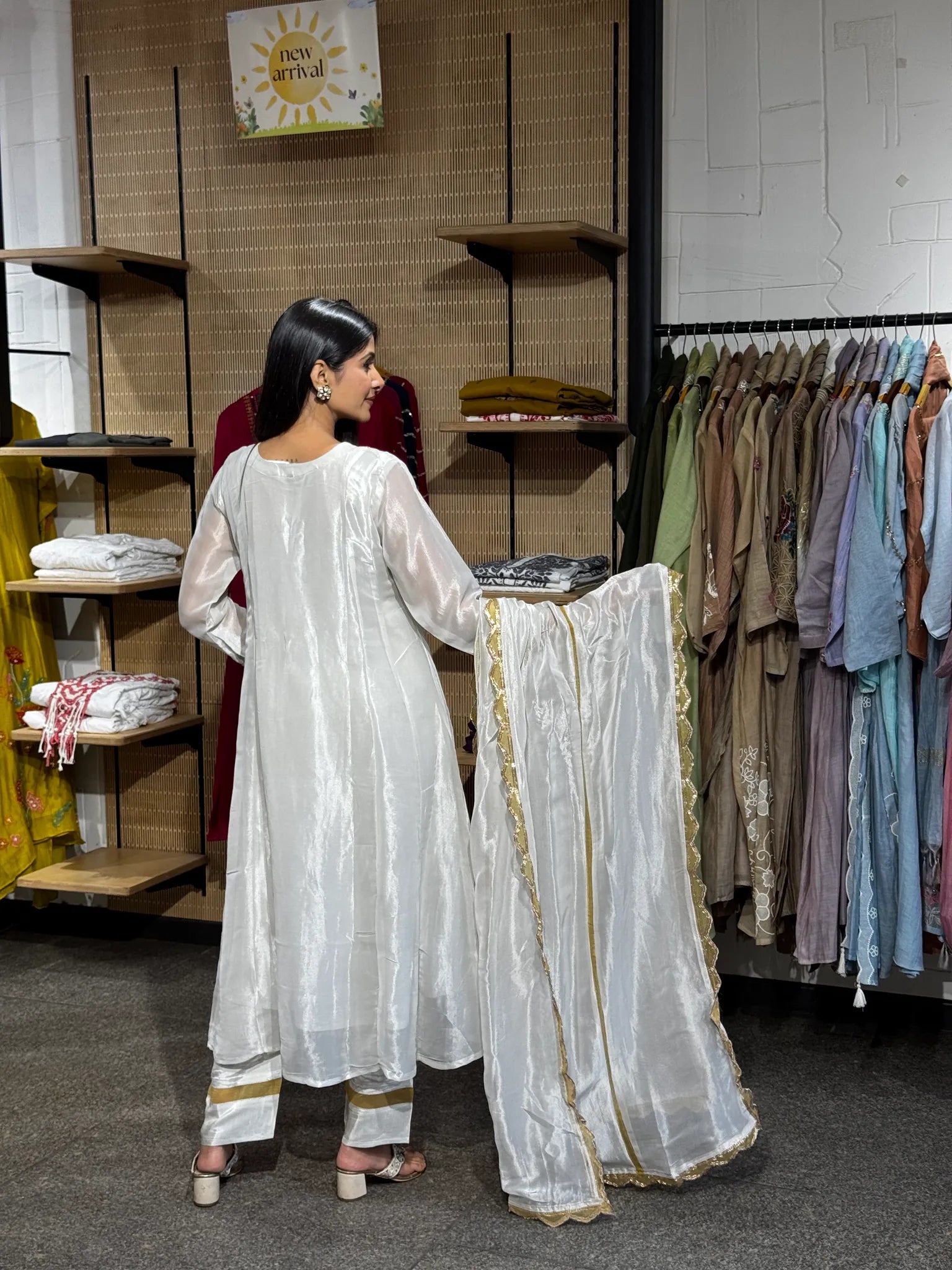 Back view of a white tissue A-line kurta and matching pants, the model holding the sheer dupatta open to show its gold edging.