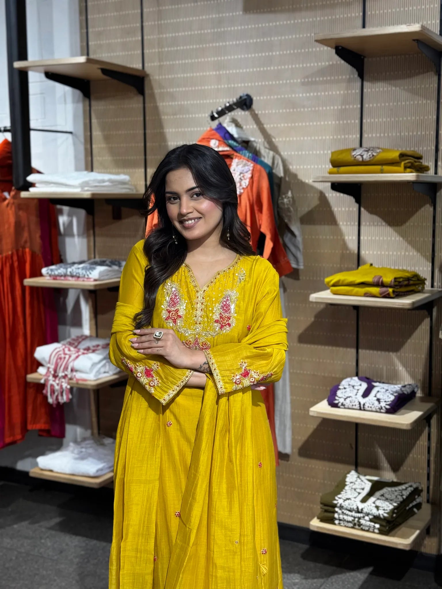 Model with arms folded, the embroidered yoke and gold-edged sleeve cuff of the mustard silk kurta in clear view.