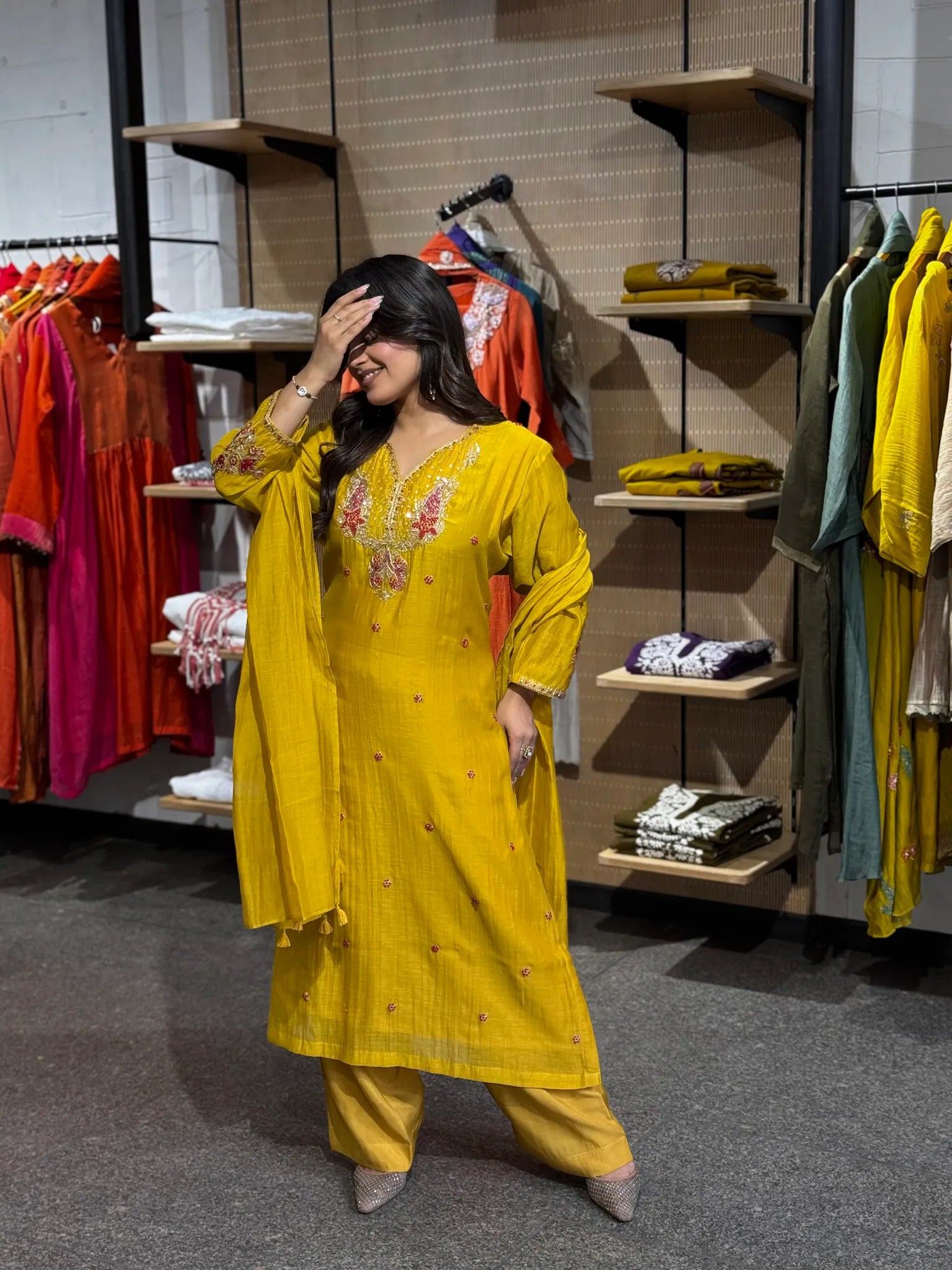 Hand raised to her brow in the mustard silk set, the sheer dupatta falling in a long line beside the flared kurta.