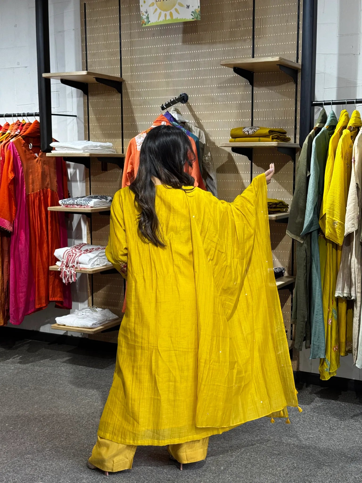 Back view of the mustard russian silk set, one arm extended so the dupatta opens out behind her in the boutique.